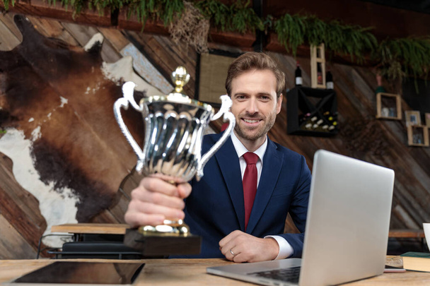 молодой бизнесмен улыбается и держит трофей и празднует победу в кофейне
 - Фото, изображение