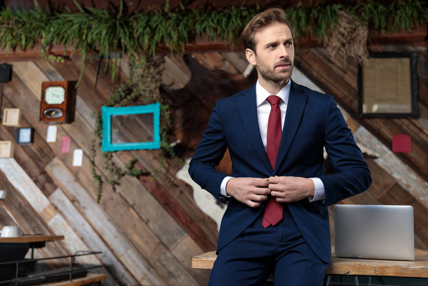 sexy zakenman aanpassen jas en op zoek naar kant, zitten in een coffeeshop - Foto, afbeelding