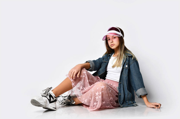 Joven modelo de chica adolescente en ropa casual elegante y zapatillas de deporte sentado y mirando a la cámara sobre fondo blanco
 - Foto, imagen