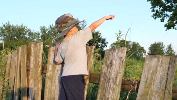 Милий хлопчик у смішному капелюсі стоїть на сільському паркані
 - Кадри, відео