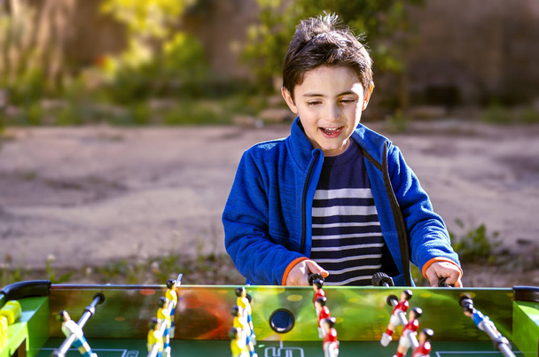Onnellinen lapsi pelaa pöytäjalkapalloa puutarhassa
 - Valokuva, kuva