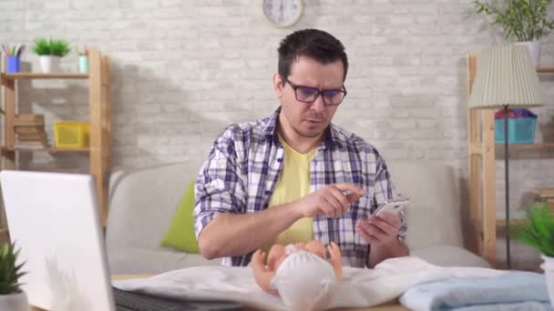 young father-to-be has problems with learning, swaddling a baby doll and looking at the camera - Filmagem, Vídeo