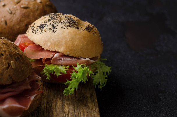 Delicious crispy burger bun with sliced ham on a vintage wooden cutting board. Dark moody food photo good for bar menu and posters. - Foto, Imagem