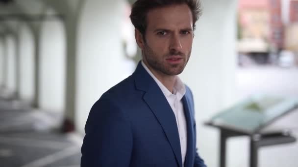 attractive businessman wearing navy suit standing and looking at camera serious and then looking away in a close up outside in the city - Materiał filmowy, wideo