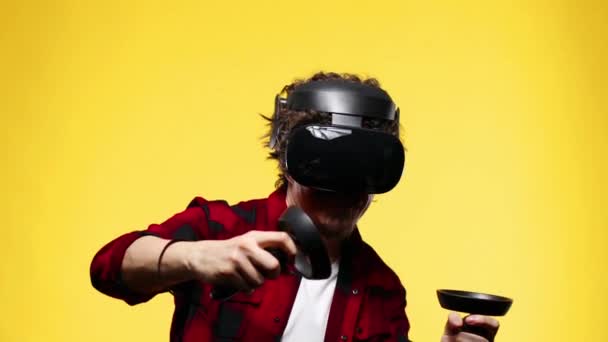 Young man with curly hair using a VR headset and experiencing virtual reality isolated on yellow background - Imágenes, Vídeo