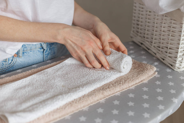 Woman rolling ironed clean towels standing at ironing board. Laundry service or cleaning housework concept - Foto, Imagem