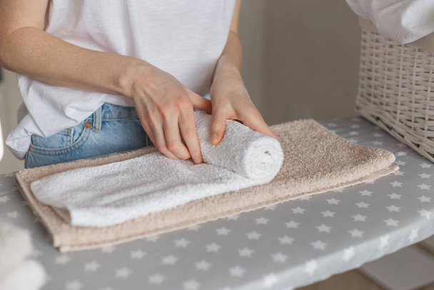Woman rolling ironed clean towels standing at ironing board. Laundry service or cleaning housework concept - Fotó, kép
