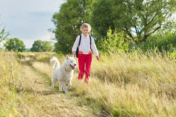 Little girl child running with white dog in meadow - Foto, imagen