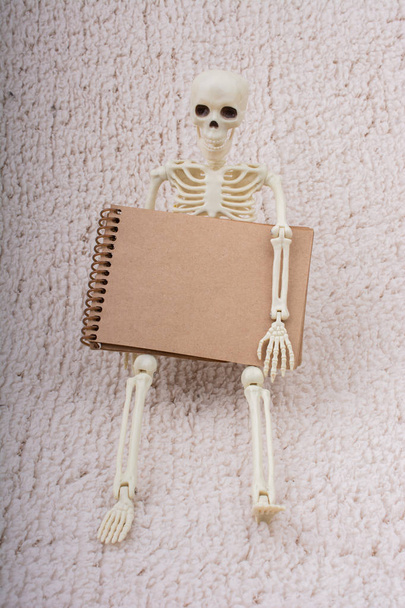 Modelo de esqueleto humano para la ciencia de la anatomía médica con cuaderno en la mano
 - Foto, imagen