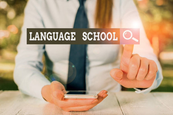 Text sign showing Language School. Conceptual photo educational institution where foreign languages are taught Female business person sitting by table and holding mobile phone. - Φωτογραφία, εικόνα