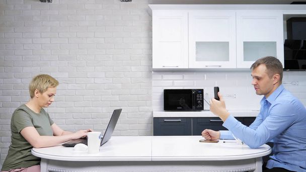 a dona de casa moderna e o homem de negócios sentam-se na cozinha, ignorando um ao outro
 - Foto, Imagem