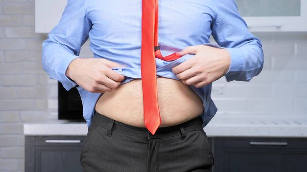 weight loss concept. man hardly fastens his pants, on a thick stomach - Foto, imagen