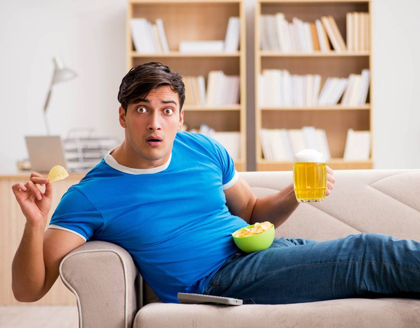 A férfi otthon focit néz, a kanapén ül. - Fotó, kép