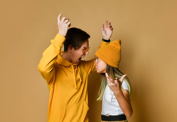 Young teens boy and girl in comfortable clothing, hats and sunglasses standing and feeling angry over yellow background - Φωτογραφία, εικόνα
