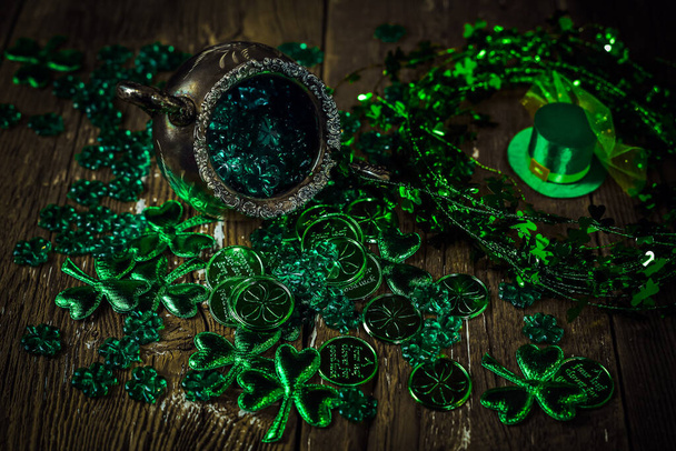 St. Patricks Day composition. Shamrocks, horseshoe, coins, leprechaun hat and silver pot on vintage style wood background. Close up view. Selective focus. Bokeh. - Photo, Image