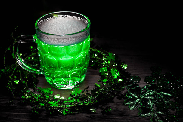 聖パトリックの日だ。シャムロックの葉で飾られた木製のテーブルの上に緑のビールのピント。緑のビールのガラスのクローズアップ。選択的フォーカス。背景がぼやけている。ぼっけ. - 写真・画像