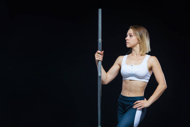 Close-up portrait of a fitness Muscular young girl posing with barbell at the gym isolated on a black background - Foto, Bild