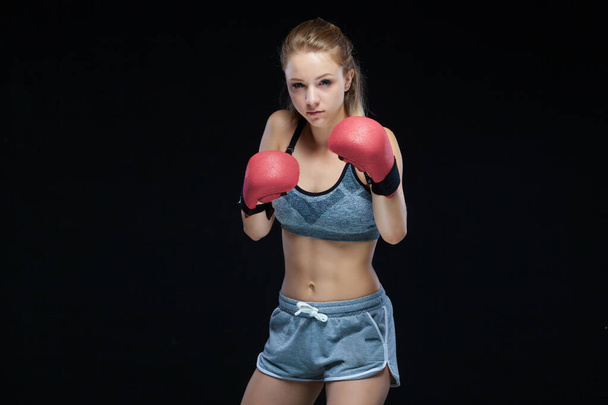 Pretty young woman posing in boxing gloves looking at camera on black background - Фото, изображение
