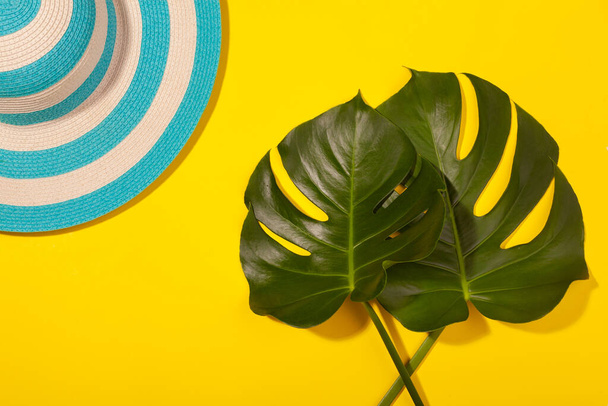 Top view on beach accessories on yellow background - striped blue hat and monstera leaves. Concept of the long-awaited vacation at sea and travel. Advertising space - Foto, immagini
