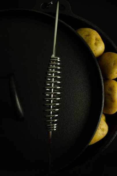 Silver handle of new dutch oven with potatoes and black background. - Zdjęcie, obraz