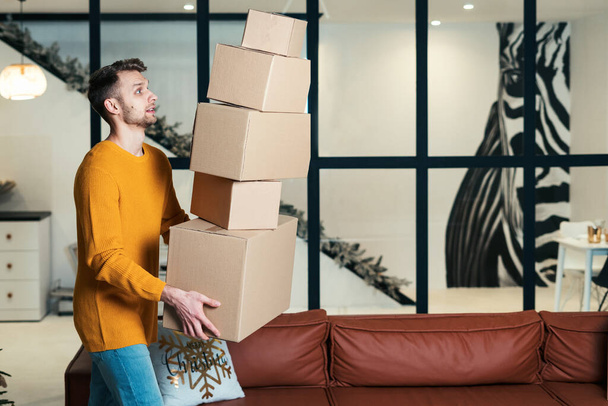 Korkmuş genç bir adamın yeni bir daireye taşınması, kutuları ellerinden bırakması, karton paketin yere düşüşüne bakması... - Fotoğraf, Görsel