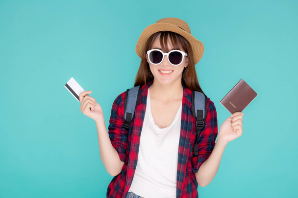 Hermosa mujer asiática joven usar sombrero y gafas de sol con mostrando tarjeta de crédito y pasaporte para viajar viaje de verano aislado sobre fondo azul, viaje de niña en vacaciones con financiación de pago en la tarjeta. - Foto, imagen