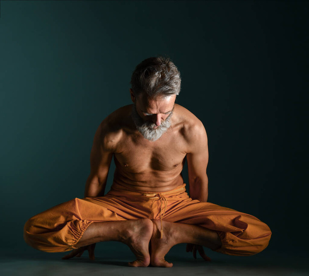 Old man with grey beard doing yoga, pilates, fitness training, stretching exercise, asana or balance workout on floor - Foto, afbeelding