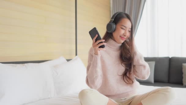 Portrait beautiful young asian woman using mobile cell phone with headphone for listen music in bedroom interior - Séquence, vidéo
