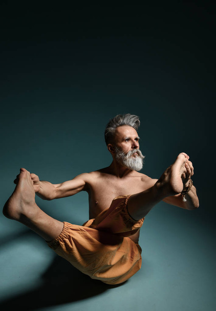 Old man with grey beard doing yoga, pilates, fitness training, stretching exercise, asana or balance workout on floor - Foto, Imagem