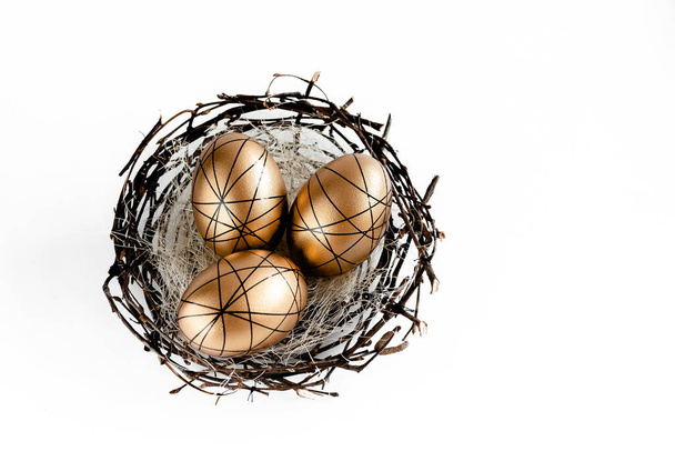 Pasen gouden versierde eieren in nest op witte achtergrond. Minimale pasen concept kopieerruimte voor tekst. Bovenste horizontale weergave, vlak. - Foto, afbeelding