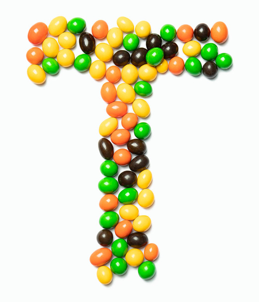 Carta T do alfabeto inglês de chocolates redondos multicoloridos sobre um fundo branco isolado. Padrão de comida feita de doces infantis. Alfabeto brilhante para design de crianças
 - Foto, Imagem