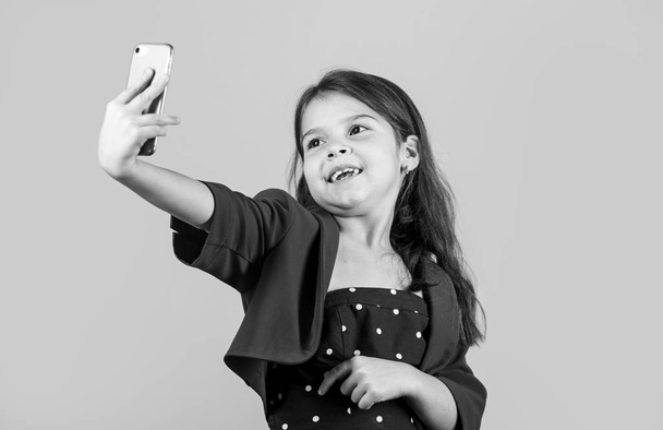 Selfie time. Small girl take selfie with smartphone yellow background. Little child selfie camera in mobile phone. Enjoying selfie session in fashion style. Communication online. Social network - Foto, Imagem