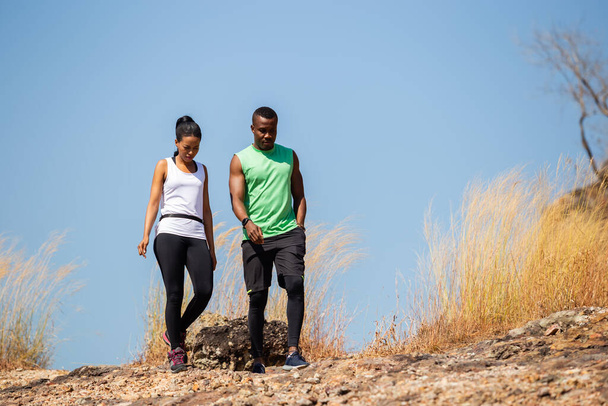 Afrykańsko-amerykańska para w odzieży sportowej spacerująca po polu po górach. - Zdjęcie, obraz