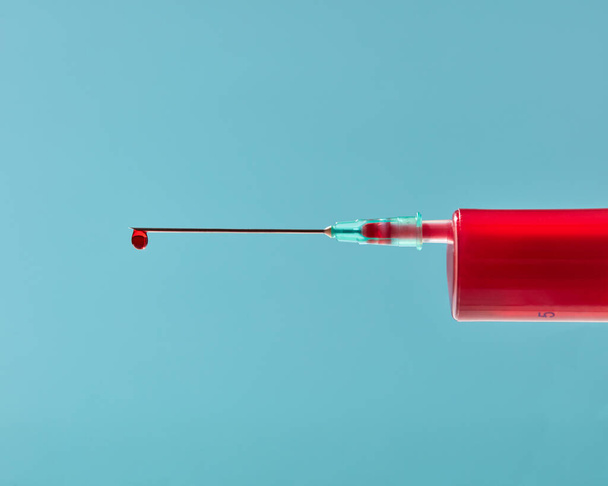 Red liquid or blood in plastic syringe with droplet on the needle on a pastel blue background, copy space. - Фото, зображення