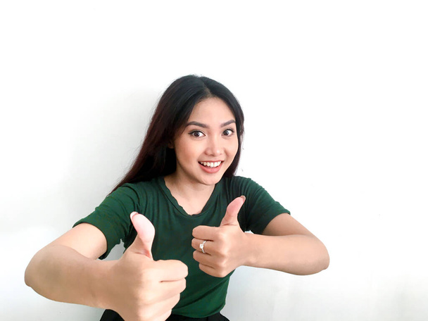 Sonriendo chica asiática en greent camiseta mostrando los pulgares hacia arriba
 - Foto, Imagen