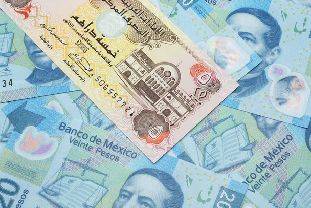 A close up image of a five dirham bank note from the United Arab Emirates on a background of Mexican twenty peso bank notes in macro - Photo, Image