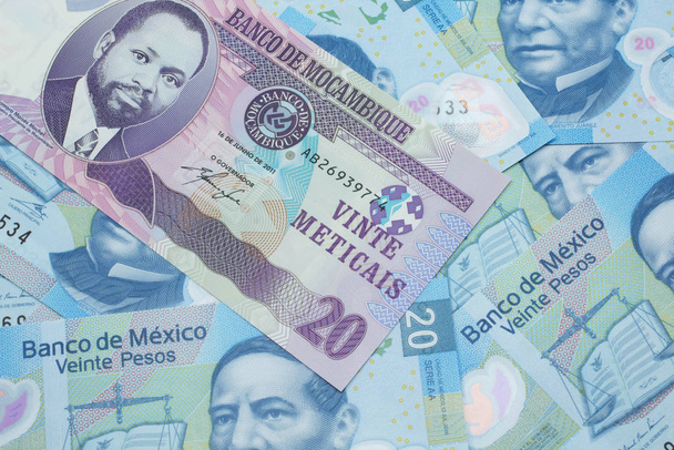 A close up image of a purple, twenty metical bank note from Mozambique on a background of Mexican twenty peso bank notes - Photo, Image