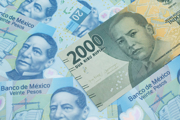Egy szürke, kétezer indonéz rúpia bankjegy mexikói húszpeso bankjegyekkel, makróban. - Fotó, kép
