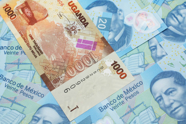 Una imagen de cerca de un colorido billete de banco de chelín ugandés con billetes mexicanos de veinte pesos en macro
 - Foto, Imagen