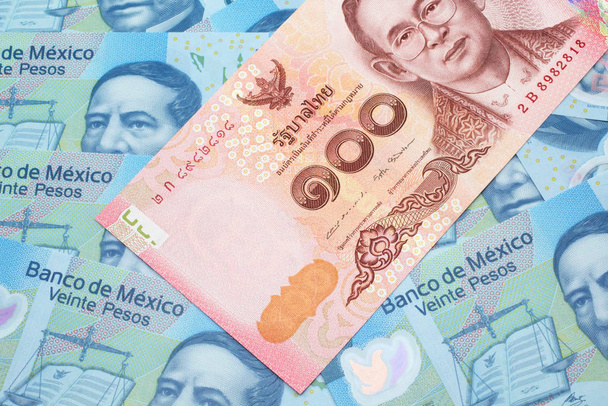 Egy közeli kép egy piros, 100 baht-os thaiföldi bankjegyről, mexikói 20 peso bankjegyekkel a makróban. - Fotó, kép