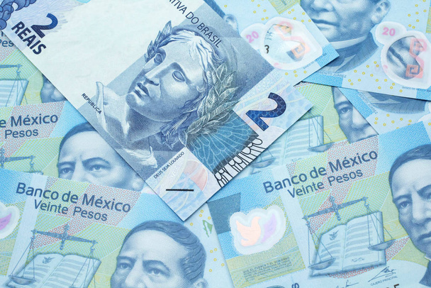 Eine blaue Zwei-Reais-Banknote aus Brasilien in Makro vor dem Hintergrund mexikanischer Zwanzig-Peso-Scheine - Foto, Bild