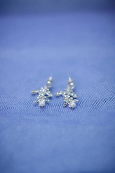 Jewelry for the bride: silver earrings with pearl beads on a blue-purple background. Selective focus. - Fotó, kép