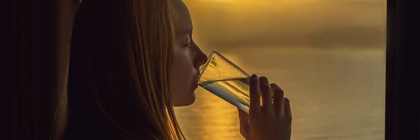 Mujer bebe agua por la mañana sobre un fondo de una ventana con vistas al mar BANNER, FORMATO LARGO
 - Foto, Imagen