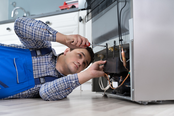Male Worker Repairing Refrigerator With Screwdriver In House - Фото, изображение