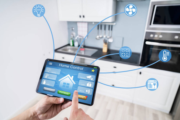 Primer plano de la mano de una persona usando la aplicación Smart Home en el teléfono inteligente en la cocina
 - Foto, Imagen