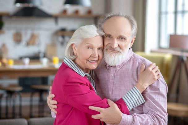 Grey-haired woman hugging her husband and looking peaceful - Φωτογραφία, εικόνα