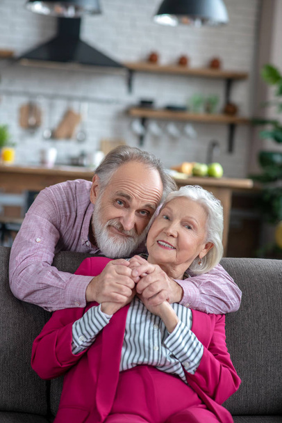 Bearded grey-haired man hugging his wife with tenderness - Foto, afbeelding