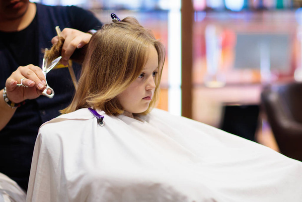Child getting haircut in beauty salon. Hairdresser cutting hair. Little girl with dark blond shoulder length bob at stylist. Kids spa. Style and fashion for children. - Photo, Image