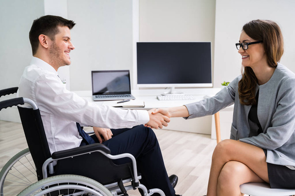 Businesswoman In Wheelchair Shaking Hands With Her Colleague In Office - Valokuva, kuva