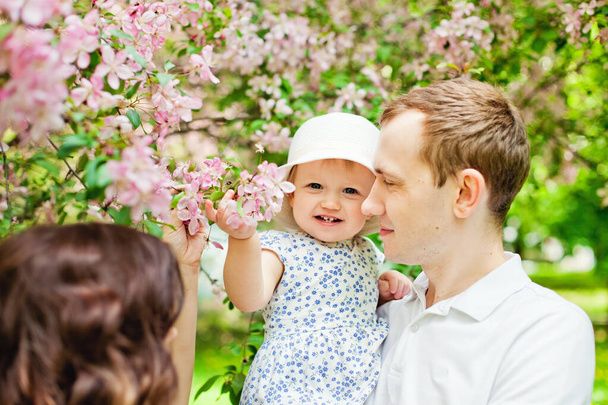 Ευτυχισμένη οικογένεια στον κήπο της άνοιξης. Μητέρα πατέρας και μικρή κόρη μαζί σε ένα ανθισμένο πάρκο Sakura. - Φωτογραφία, εικόνα